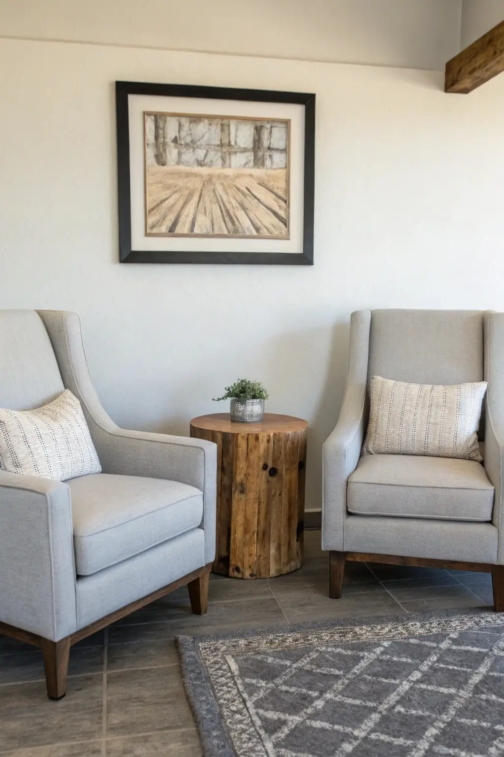 Modern farmhouse living room seating arrangement with two light grey armchairs, a reclaimed wood side table, and neutral abstract art.
